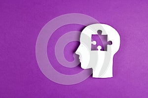 Human head paper silhouette with a puzzle piece cut out on the purple background. Mental health symbol