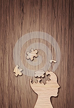 Human head silhouette with a jigsaw piece cut out on the wooden background, mental health concept.