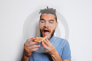 Human holds piece of cheese pizza with tomatoes in his hands and enjoys eating. Young cute Caucasian man with beard and dreadlocks