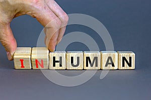 Human or inhuman symbol. Businessman turns wooden cubes and changes the word inhuman to human. Beautiful grey table grey