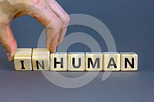 Human or inhuman symbol. Businessman turns wooden cubes and changes the word inhuman to human. Beautiful grey table grey