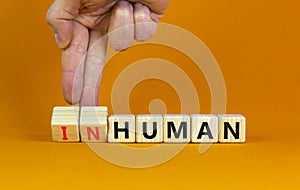 Human or inhuman symbol. Businessman turns wooden cubes and changes the word inhuman to human. Beautiful orange table orange