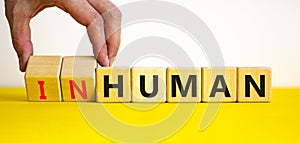 Human or inhuman symbol. Businessman turns wooden cubes and changes the word inhuman to human. Beautiful yellow table white