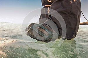 Human legs in hiking boot in ice crampons on the texture Baikal