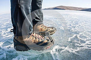 Human legs in hiking boot in ice crampons on the texture Baikal