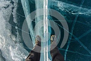 Human legs in hiking boot in ice crampons on the texture Baikal ice