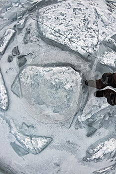 Human legs in hiking boot in ice crampons on the texture Baikal ice