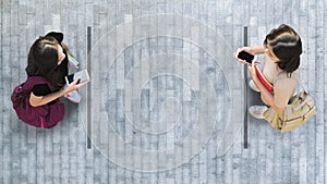 Human life in Social distance. Aerial top view with two student women with smartphone stand at grey pavement street road with