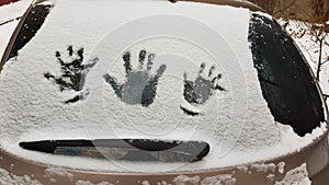 Human palm`s imprints into white snow covered windshield glass of car. Kid`s and adult`s handprints closeup. Concept of winter.