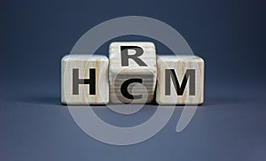 Human resource and capital management symbol. Turned wooden cubes and changed the word HCM to HRM. Beautiful grey background.