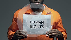 Human rights phrase on cardboard in hands of African-American prisoner, assault