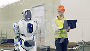 A human and a robot walk together at a warehouse, close up.