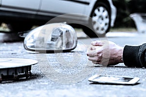 Human`s hand on the ground next to broke car mirror and mobile phone after a crash