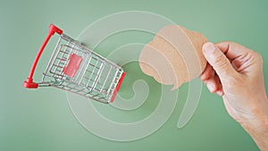 Human`s hand holding grunge brown speech bubble with blurred shopping cart on green background, chat or online order
