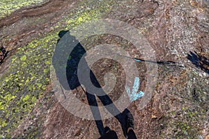 Human shadow walking in wrong direction, against blue arrow on rock