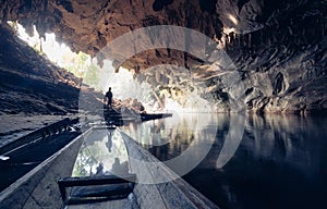 Human silhouette stands inside water cave with torch in hand in Konglor, Laos