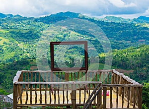 Human Size Wooden Picture Frame on a Platform With Background of A Green Forest and Mountains In A Sunny Clear Blue Sky