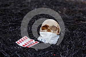 A human skull on a black background of burnt grass with red capsules of medical drugs.