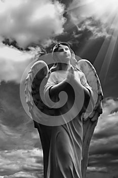 Human soul as angel with wings looking up at the sky in rays of light. Ancient statue. Black and white image