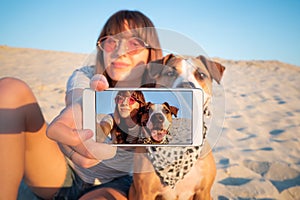 Human taking a selfie with dog. Best friends concept: young female makes self portrait with her puppy outdoors on a beach