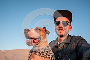 Human taking a selfie with dog on sandy beach. Happy young male
