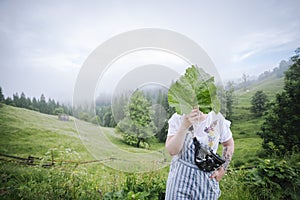 Human with tattooed sleeve standing in the cloudy mountains and hiding it`s face with a big green leaf - beautiful allegory about