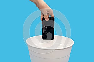 Human throws a broken mobile phone into a trash can on a blue background