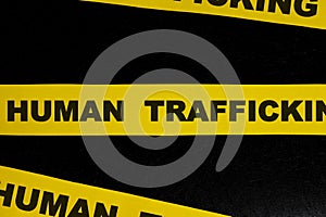 Human trafficking caution and warning concept. Yellow barricade tape with word in dark black background.