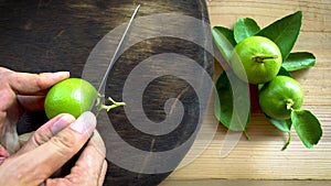 Human using kitchen knife slice cut green lemon on wood cutting board