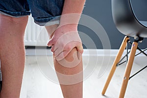 Human, who had been elevated from chair, holding his palm over calf or gastrocnemius muscle, which grabbed cramp with severe pain. photo