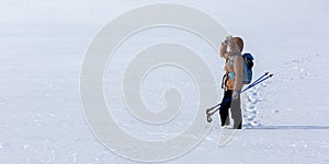 Human in winter clothes standing in a snowy field with ski poles in hand and looking ahead in winter day, format 1x2