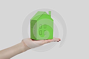 Human woman hand holding and showing green paper house model. in