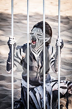 A human zebra woman crouches down behind cage bars