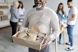 Humanitarian aid. African american elderly man holding box with donations food, volunteers packing boxes with products