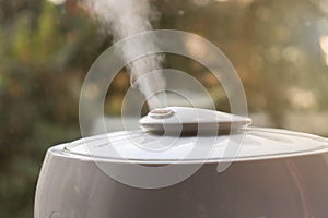 Humidifier producing a vapor into a room standing on a windowsill against sunlight