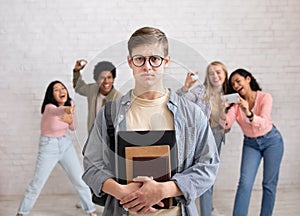 Humiliation and bullying at school. Focus on sad young guy in glasses and notebooks