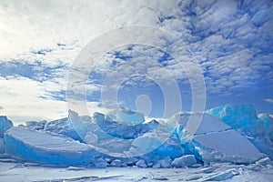 Hummocks of turquoise blue ice blocks under white clouds