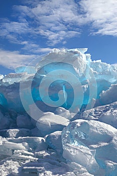 Hummocks of turquoise blue ice blocks under white clouds, vertical