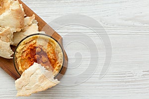 Hummus in bowl with roasted chickpeas, paprika, olive oil and pita bread on rustic wooden board over white wooden background, top