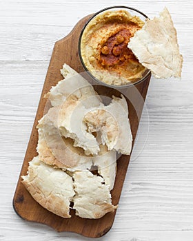 Hummus in bowl with roasted chickpeas, paprika, olive oil and pita bread on rustic wooden board over white wooden background, top