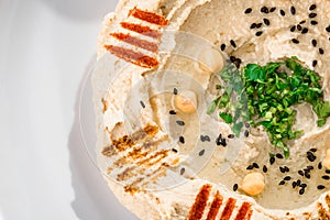 Hummus with greens in a round white plate on a light wooden background among fresh vegetables