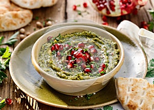 Hummus. Herb hummus with the addition of pomegranate seeds, parsley, olive oil and aromatic spices in a ceramic pot on a wooden