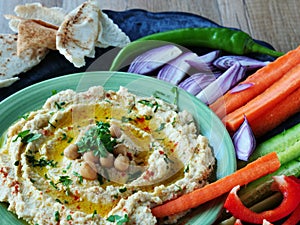 Hummus topped with whole chickpeas and olive oil served with vegetables
