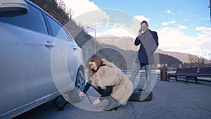 Humor. woman changing a car wheel. man talking on the phone
