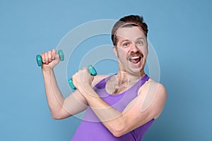 Humorous athletic man using small dumbbells for bodybuilding