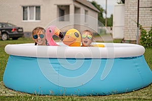 Humorous girls look out of a small inflatable swimming pool in the yard at home