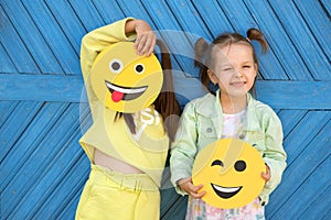 Humorous kids hold various smile faces and make faces standing at blue wall