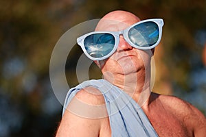 Humorous portrait of an adult bald man in a blue toga and funny blue glasses.