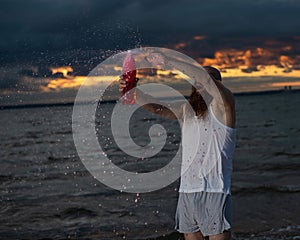 A humorous portrait of a brutal man pouring soda from a bottle on the beach at sunset