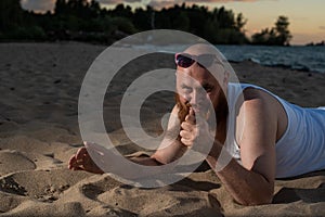 A humorous portrait of a brutal man in a T-shirt and boxers on the beach at sunset